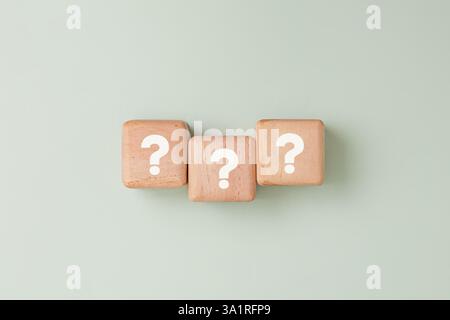 Three wooden blocks with white question marks in straight line against light pale green background. Symbolizing for concepts like problem-solving Stock Photo
