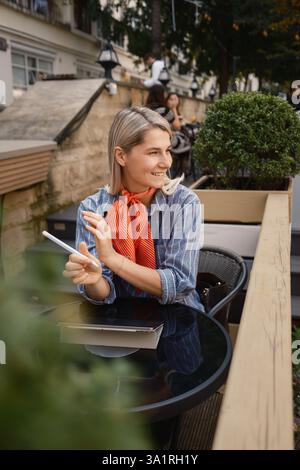 Smiling woman working outdoors at a cozy cafe with tablet Stock Photo