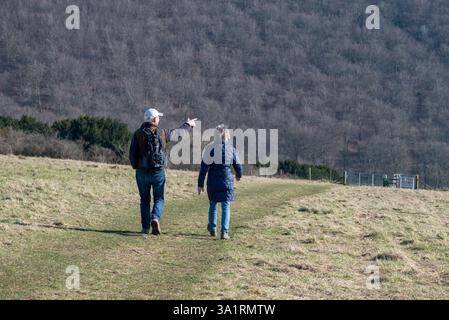 An elderly couple hiking down Butser hill, both wearing warm clothing and walking boots. The man pointing to something in the distance. March 2025. Stock Photo