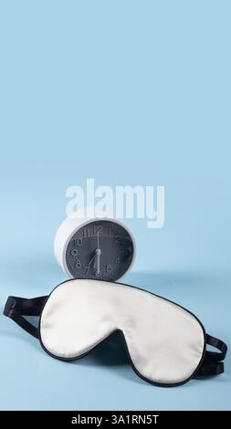 White silk sleeping mask and alarm clock isolated on pastel blue background. World sleep day concept Stock Photo