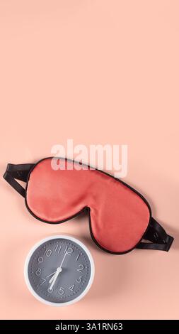 Bright pink sleeping mask and alarm clock isolated on plain warm pink background. World sleep day concept Stock Photo