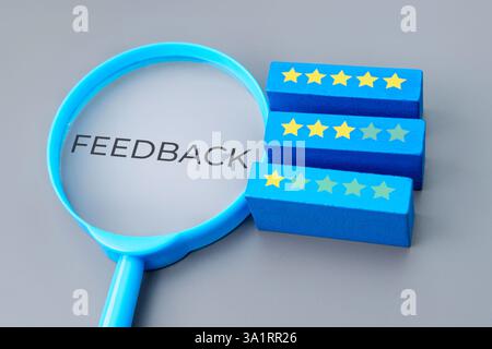 A magnifying glass with the word "FEEDBACK" next to three blue blocks displays yellow star ratings. Testimonial, review concept. Stock Photo