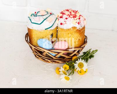 Sweet Easter cakes and colorful Easter eggs in the wicker basket with a white wall on the background. Stock Photo