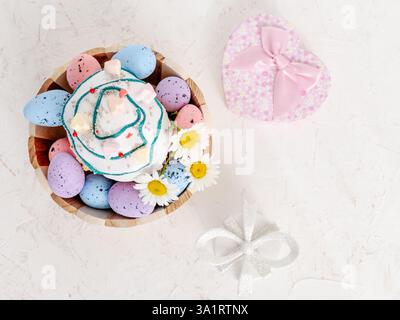 Sweet Easter cake and colorful Easter eggs in the wooden basket with gift boxes on the white background. Top view. Stock Photo