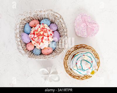 Sweet Easter cakes and colorful Easter eggs in the wooden baskets with gift boxes on the white background. Top view. Stock Photo