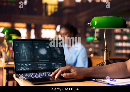 African american med school pupil studies pharmacology notes in a library, preparing for exams and advancing their healthcare career. Man in scrubs works hard on medical school success. Stock Photo