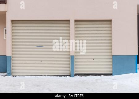 Two closed garage doors on a building with snow on the ground Stock Photo