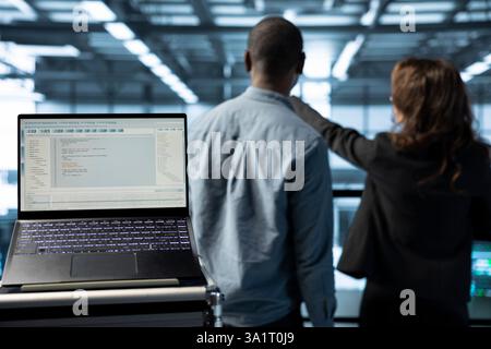 Focus on lines of code on laptop screen used by data center engineers in blurry background to execute security patches. Close up of script on notebook ran by server hub employees scanning equipment Stock Photo