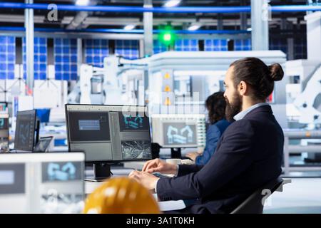 Engineer in solar panel manufacturing facility reviewing photovoltaic system performance on PC. Specialist analyzing production metrics to optimize efficiency in industrial renewable energy plant Stock Photo