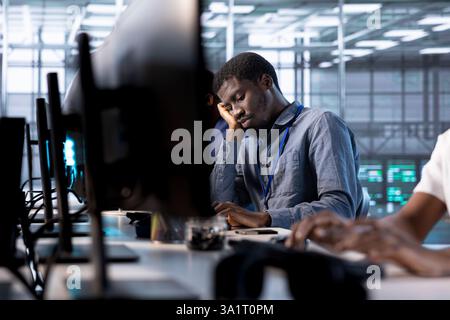 Bored data center engineer mindlessly using programming languages to construct algorithms and build applications. Fatigued server room employee tired of debugging and optimizing code Stock Photo