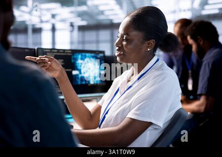 Smiling woman talking with colleague in server room, creating high performance AI systems on PC. Cheerful admin in data center discussing with coworker, developing artificial intelligence Stock Photo