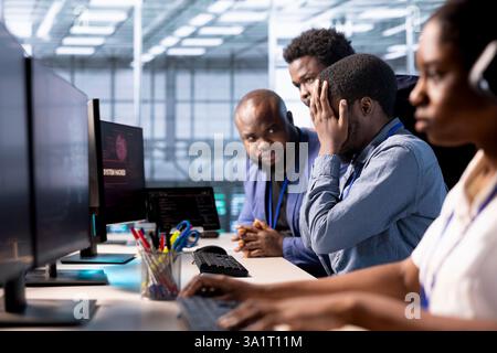 Team of programmers in server farm upset after losing all data after hacker managed to pass firewall. Critical error alert on monitor in data center making IT staff members feel dejected Stock Photo