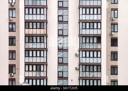 The facade of a multi-storey residential building. Many windows. Background wall of a tall brick house with glass windows. Stock Photo