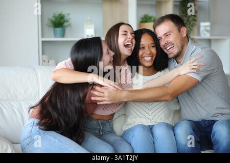 Four diverse happy friends hugging sitting on a sofa at home Stock Photo