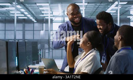 Data center coworkers laughing, having fun while maintaining company network infrastructure. Server hub colleagues enjoying time together in office, telling jokes, having conversation, camera A Stock Photo