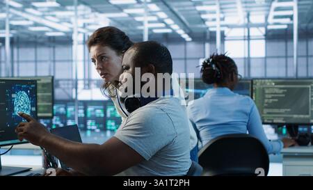 Teamworking colleagues updating AI systems, writing intricate binary code scripts on PC and laptop. Team of engineers using programming to upgrade artificial intelligence simulation model, camera A Stock Photo