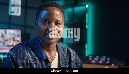Jolly freelancer noting down ideas on paper using pen while teleworking. Upbeat remote employee working at home office desk, reading information on laptop and writing in notebook, camera B Stock Photo