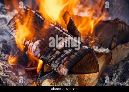 Close-up of wood burning with bright flames consuming the surface, revealing glowing embers, deep cracks, and intense heat Stock Photo