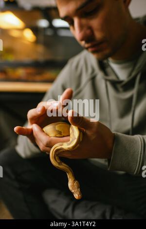 Young man gently holding a pet snake near its reptile habitat Stock Photo