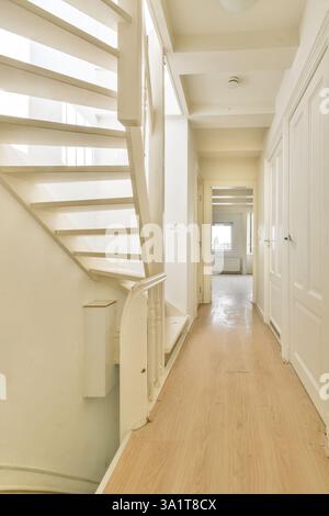 A spacious hallway featuring a bright staircase with minimalist design. The wooden flooring adds warmth while the white walls create an airy atmosphere. Stock Photo