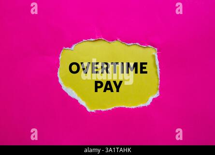 Overtime pay message written on ripped torn pink paper on yellow background. Conceptual overtime pay symbol. Copy space. Stock Photo