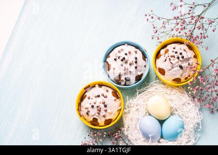 Delicious Easter cupcakes and eggs on a light blue background with flowers. Easter cakes with glaze in bright baking molds of yellow and sky color. Co Stock Photo