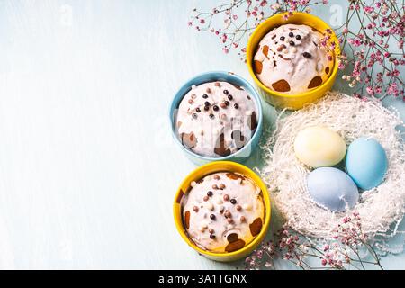Delicious Easter cupcakes and eggs on a light blue background with flowers. Easter cakes with glaze in bright baking molds of yellow and sky color. Co Stock Photo