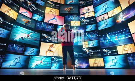 Elderly woman looking at multiple screens displaying generated sports visuals on futuristic digital wall. Stock Photo