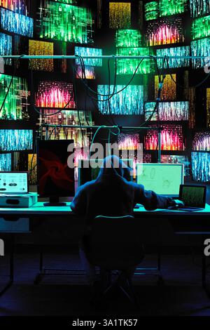 Hacker working on multiple devices while encrypted data flows across digital walls. Stock Photo