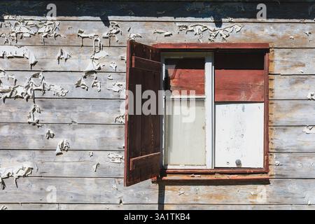 close-up of an old wooden window with a partially open red shutter on a weathered wooden wall Stock Photo