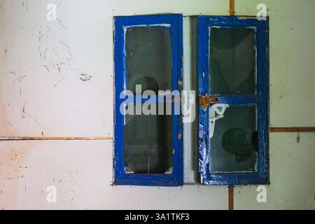 close-up of an old wooden window with a partially open blue shutter on a weathered wall Stock Photo