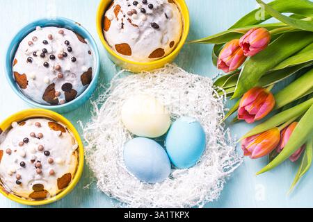 Easter cakes, painted eggs in the nest and tulips on a blue background. Flat layout. View from above. High quality photo Stock Photo
