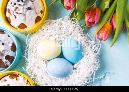 Easter cakes, painted eggs in the nest and tulips on a blue background. Flat layout. View from above. High quality photo Stock Photo