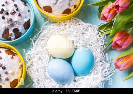 Easter cakes, painted eggs in the nest and tulips on a blue background. Flat layout. View from above. High quality photo Stock Photo