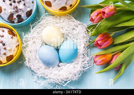 Easter cakes, painted eggs in the nest and tulips on a blue background. Flat layout. View from above. High quality photo Stock Photo