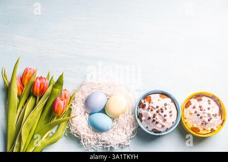 Easter cakes, painted eggs in the nest and tulips on a blue background. Flat layout. View from above. High quality photo Stock Photo