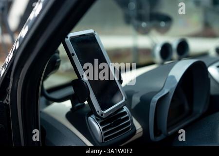 Modern smartphone device gadget mounted on phone holder at car dashboard. Mock-up white screen isolated template. Copyspace for text . Vehicle Stock Photo