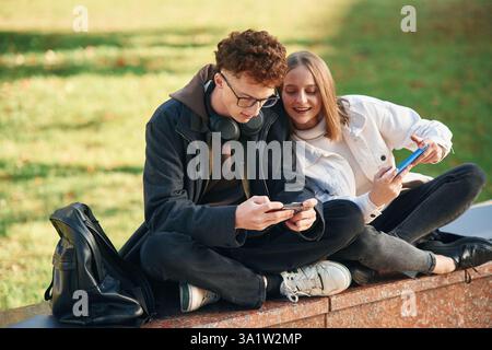 Playing games by using smartphones. Two young students are together outdoors. Stock Photo