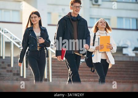 Walking down the stairs. Three young students are outside the university outdoors. Stock Photo