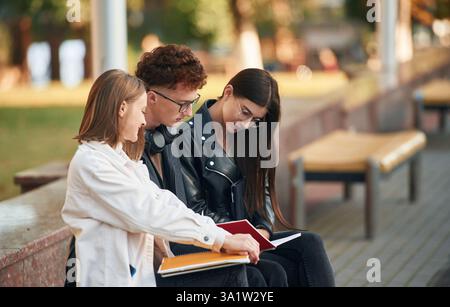 Sitting together. Three young students are outside the university outdoors. Stock Photo