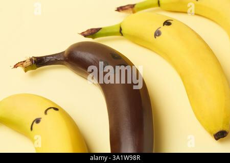 Stop racism. One dark banana among yellow ones on beige background, closeup Stock Photo