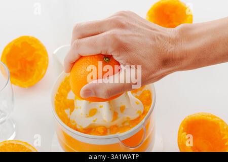 closeup of a man making an orange juice with an electric juicer, on a white surface Stock Photo