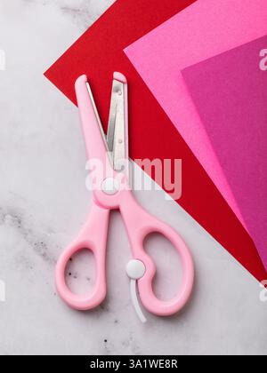 Children's pink scissors and colored paper on table, top view Stock Photo
