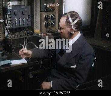 Italian Senator Guglielmo Marconi Using Radio Apparatus While Taking Notes, 1920. 'Signor Marconi, the radio expert. His work in the past had revolutionised wartime naval operations. Now, what new marvel was to come next? Messages to the Moon, some claimed'. From "Time To Remember - The Plunge Into Peace", 1920 (Reel 4); events of 1920 - weddings, women's rights, industrial unrest and problems in Ireland. (Colorised black and white still) Stock Photo