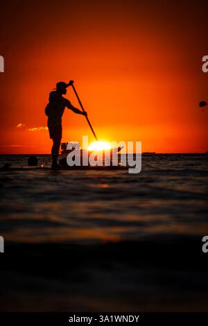 Silhouette of a person paddleboarding on calm water during a vivid sunset at White Beach, Boracay, Philippines Stock Photo