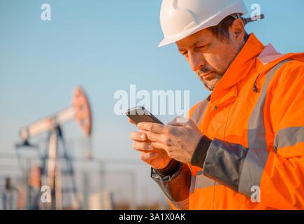 Drilling rig engineer using mobile phone while supervising the process of oil and gas, monitoring rig performance in field, selective focus Stock Photo