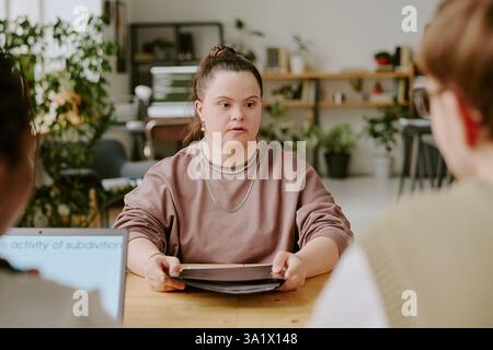 Medium close up of young woman with down syndrome holding resume while sitting at table during job interview Stock Photo