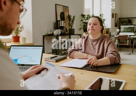 Medium close up of young woman with down syndrome sitting at table in front of job interiview who reading her cv Stock Photo