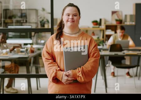 Portrait of smiling female office worker standing in office and holding gray clipboard Stock Photo