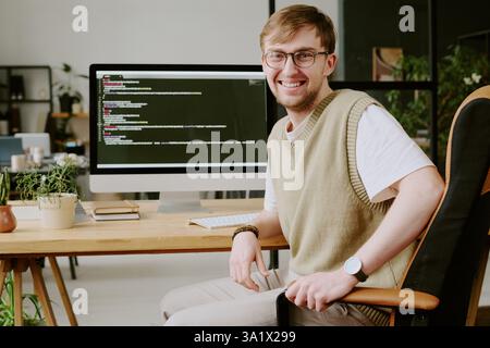 Portrait of smiling and confident young man sitting in chair posing for photo while spending work day in office Stock Photo